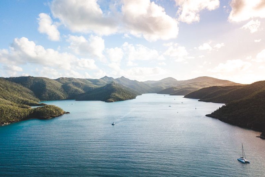 Aerial landscape of the Whitsunday Islands with calm blue water, anchored sailboats and lush green mountains at sunset in Queensland, Australia.