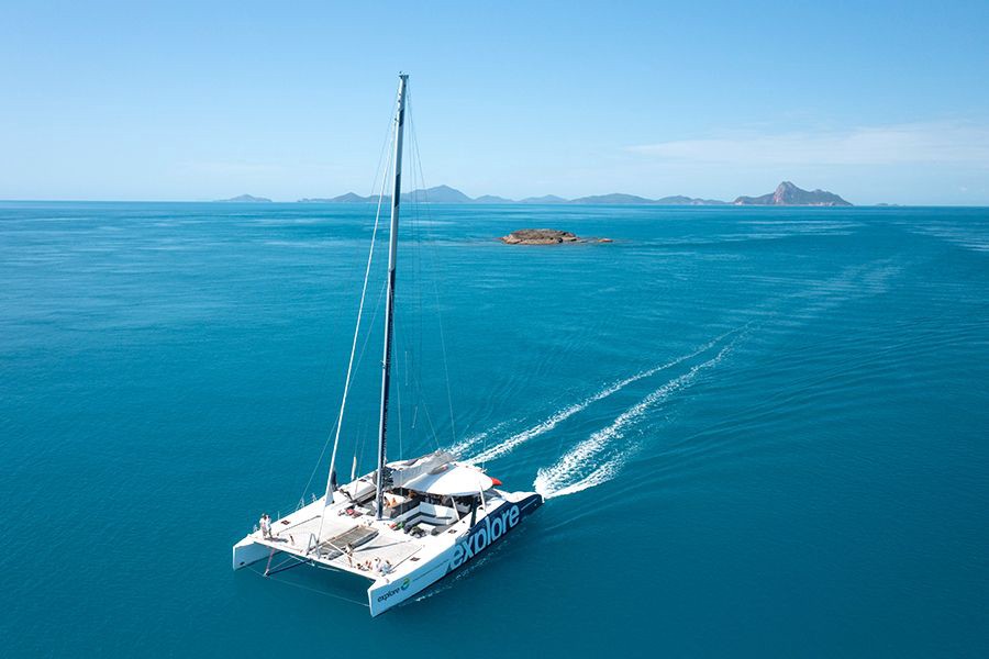 Aerial view of the Explore Whitsundays catamaran cruising across turquoise waters near tropical islands in the Whitsundays, Queensland, Australia.
