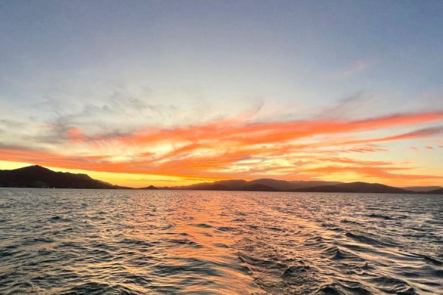 Vibrant orange and pink sunset over the ocean with silhouetted island mountains in the Whitsundays, Queensland, Australia.