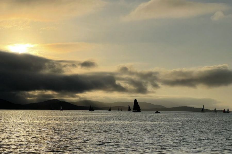 Silhouetted sailboats scattered across calm ocean waters under a moody sunset sky in the Whitsunday Islands, Queensland, Australia.