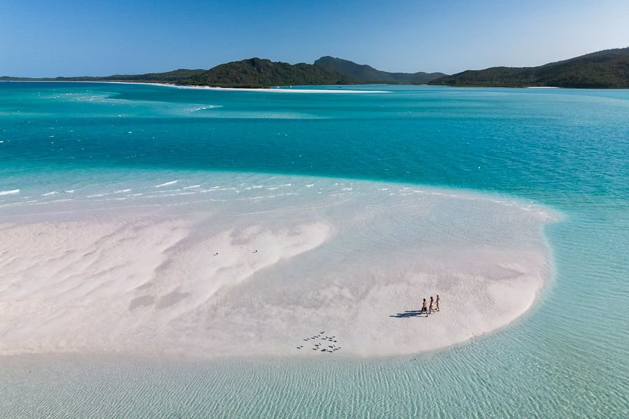 three people walking on a patch of sand at Whitehaven Beach and its swirling sand formations