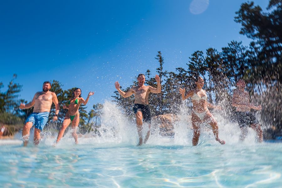 Group of friends running into shallow turquoise water on the beach while laughing and splashing