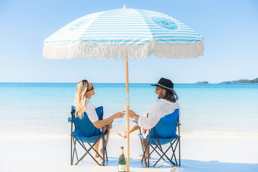couple sitting in beach chairs under a beach umbrella on a beautiful white sand beach