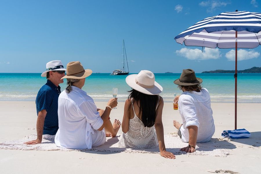 group of four relaxing on the white sand of whitehaven beach on an overnight whitsundays sailing tour