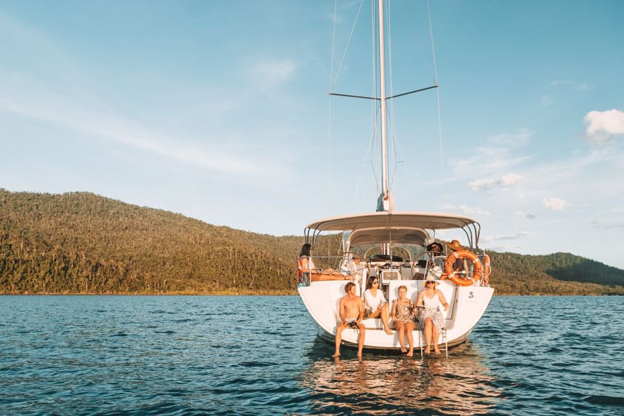 rear view of blizzard sailing yacht with guests gathered around the seating areas, whitsunday mountains in the background