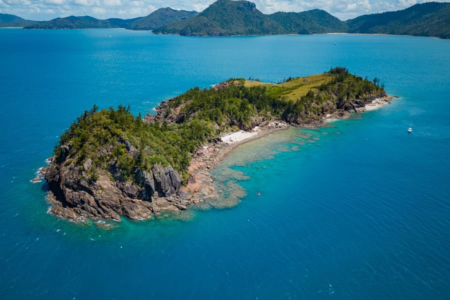 Aerial view of a small rocky island with turquoise water and fringing reef in the Whitsundays, Queensland
