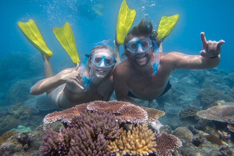 Two snorkellers with snorkel gear smiling while floating above corals reefs underwater