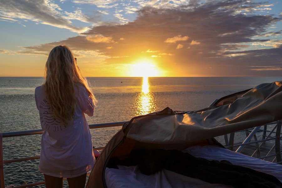 woman taking a photo of the sunrise next to an outdoor reefbed on Reefsleep