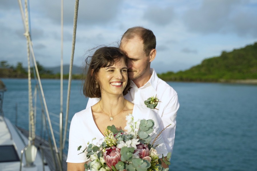 couple dressed in white holding flowers posing on a private tallship charter for a wedding in whitsundays