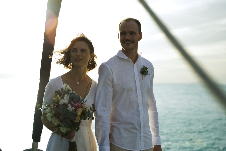 Couple standing on the deck of a private yacht charter in the sunshine during a wedding ceremony